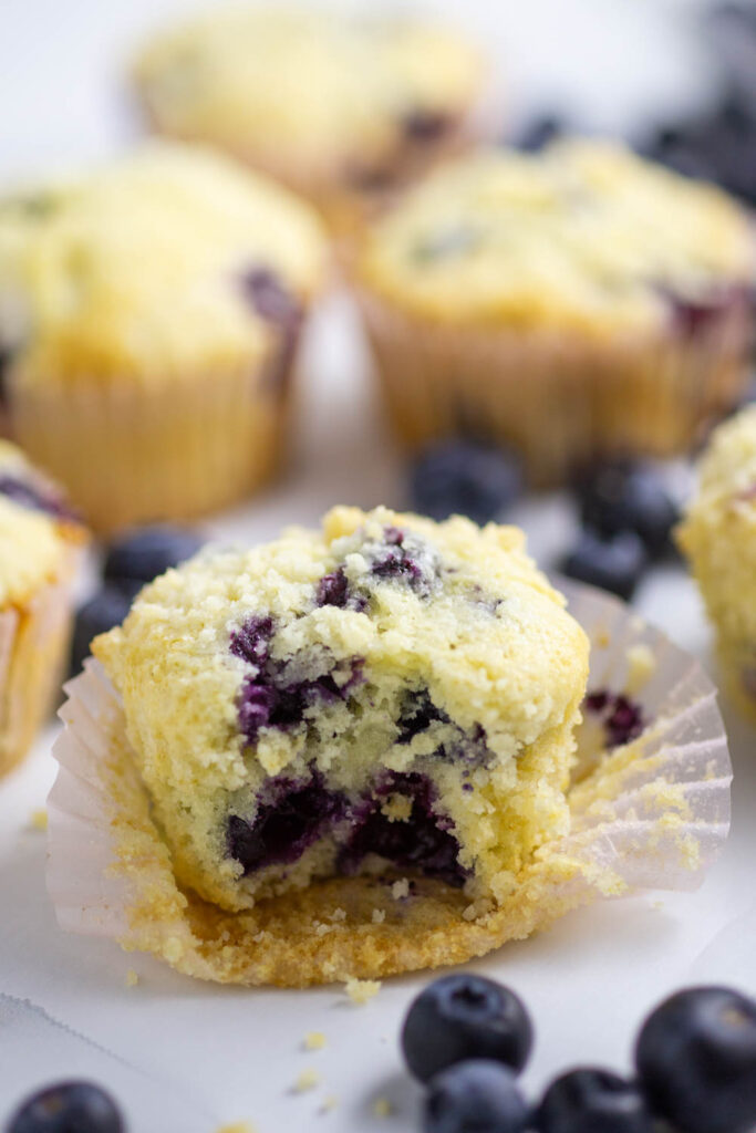 blueberry muffin with a bite taken out and blueberries showing in the center with blueberries in front and more muffins behind.