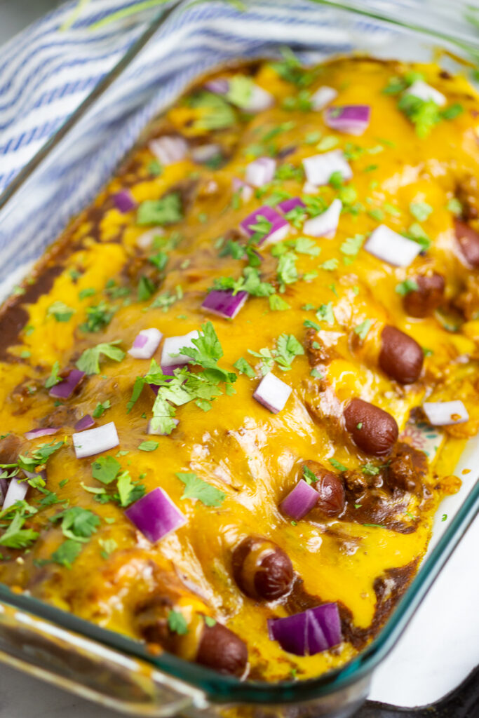 Chili cheese dog casserole in a glass 9-inch by 13-inch casserole dish topped with cilantro and red onions