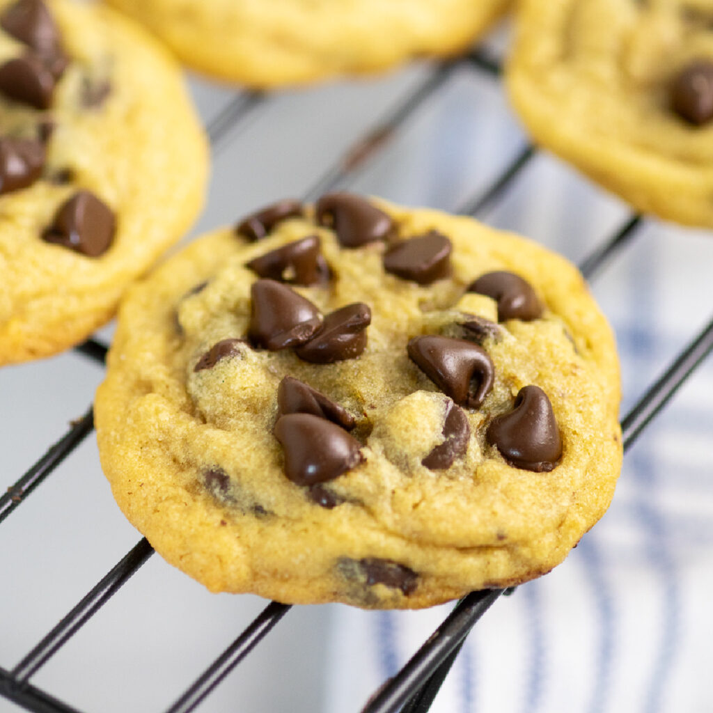 Bakery Style Chocolate Chip cookie on a wire cooling rack with more cookies behind.