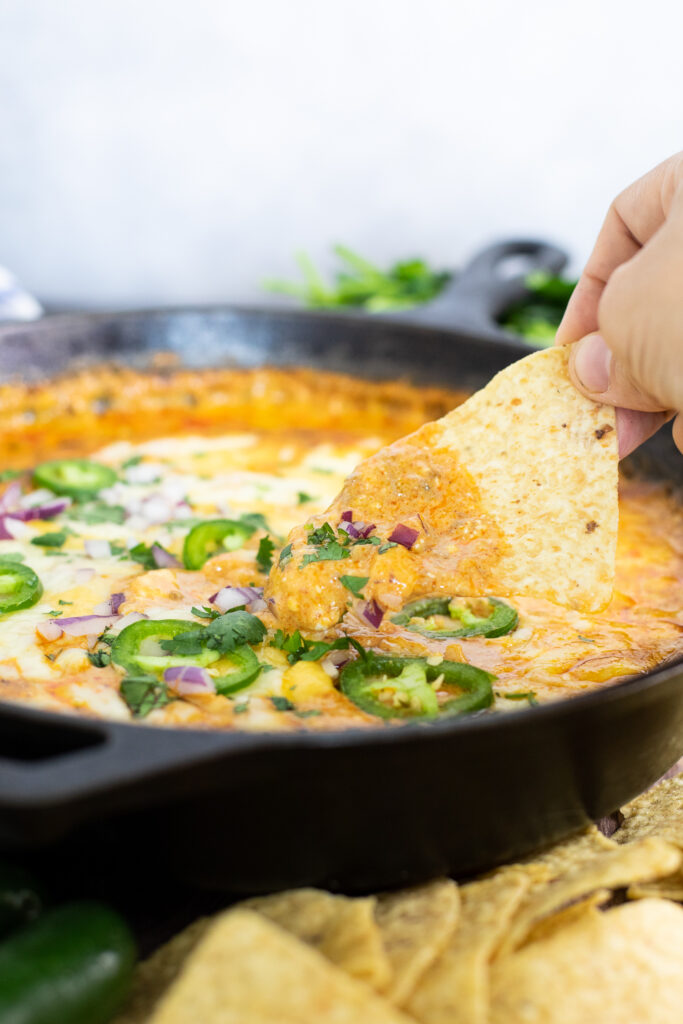 Tortilla chip dipping into a skillet of gooey easy chili cheese dip