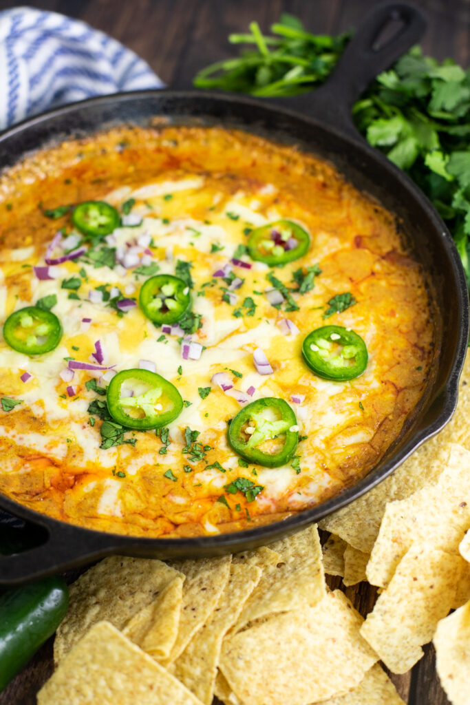Skillet filled with cheesy easy chili cheese dip topped with fresh jalapeno slices, diced red onion, and chopped cilantro