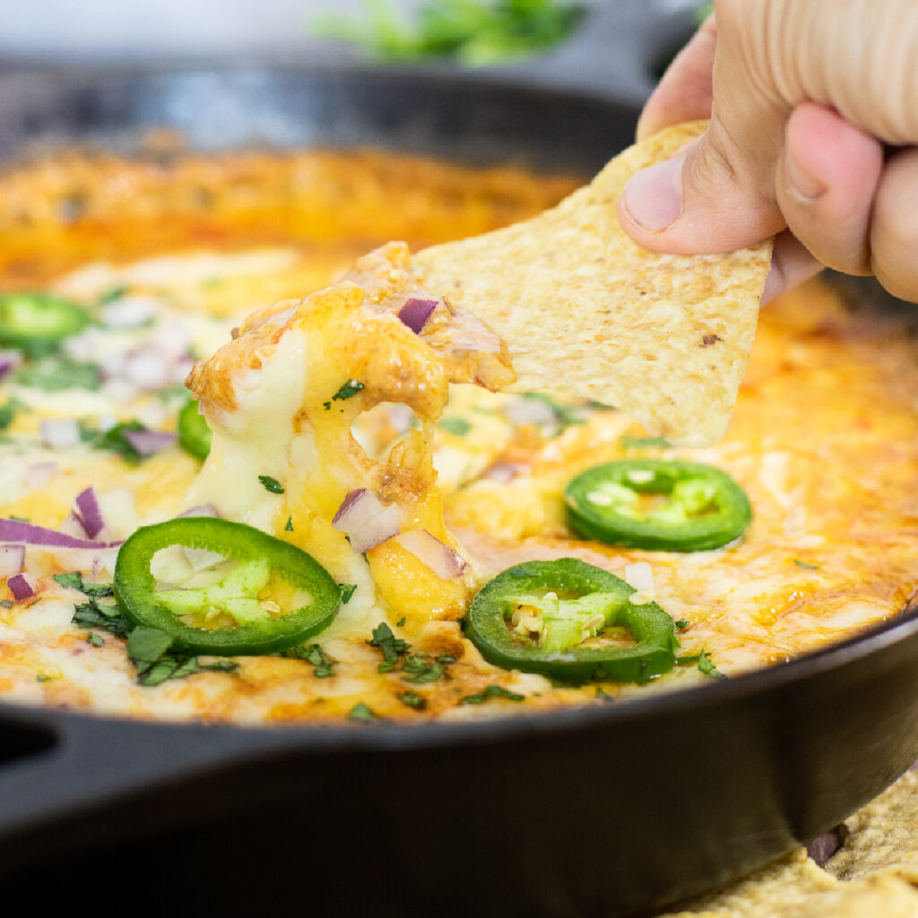 Tortilla chip dipping into a skillet of gooey easy chili cheese dip