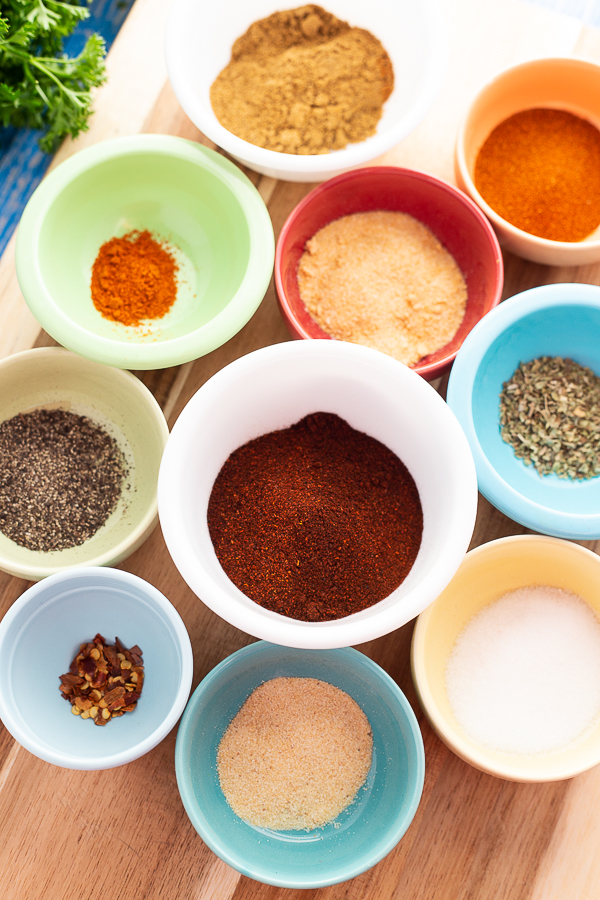 Spices for homemade taco seasoning in small colorful bowls sitting on a wooden cutting board