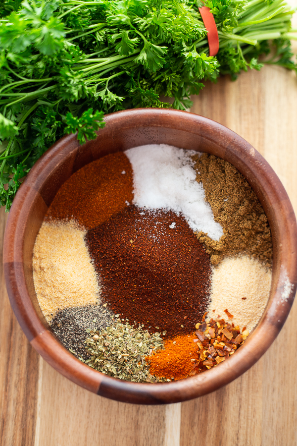 Homemade taco seasoning spices in one wooden bowl, unstirred, sitting on a wooden cutting board with cilantro