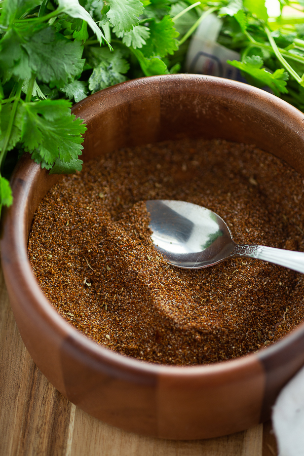 Homemade taco seasoning in a wooden bowl with a spoon it and cilantro in the background