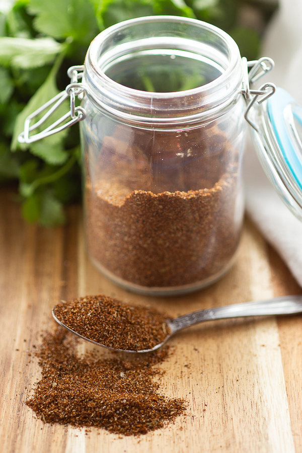 Taco seasoning in a little jar with a spoon full of seasoning in front.