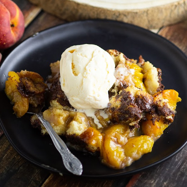 Peach cobbler on a plate topped with ice cream with a spoon