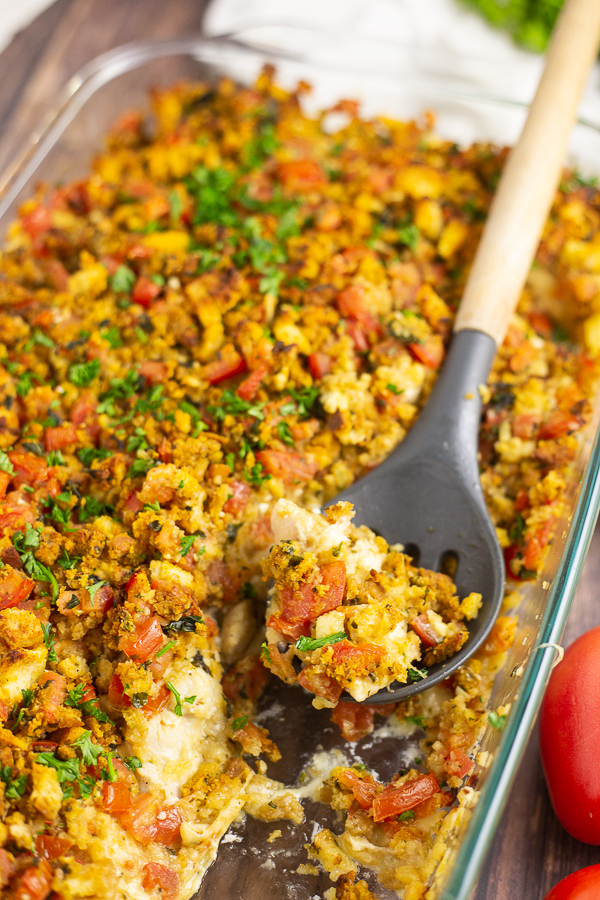 Casserole dish filled with bruschetta chicken bake with a spoonful missing and a wooden spoon in the dish.
