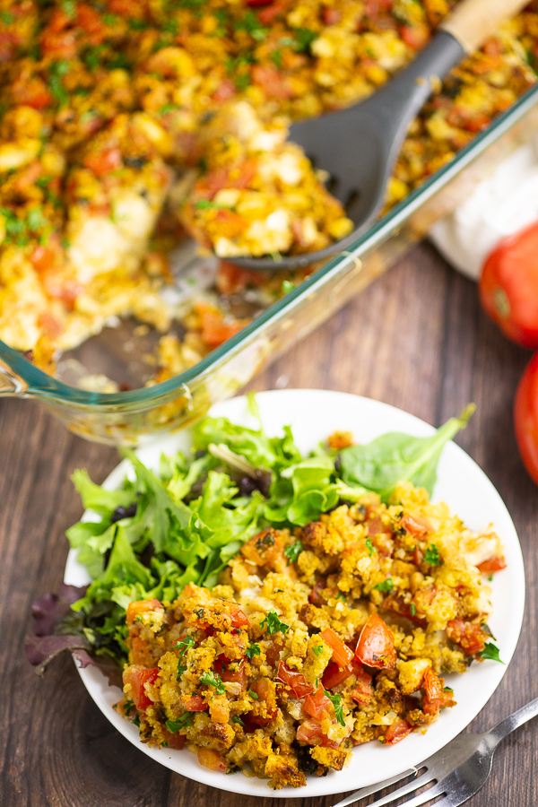 A scoop of bruschetta chicken bake on a small plate with a green salad and the rest of the casserole in the casserole dish behind it