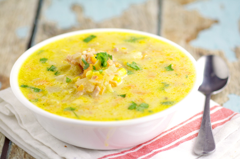 Cheesy ham and corn chowder in a white bowl on a wooden background with a white and red napkin and silver spoon