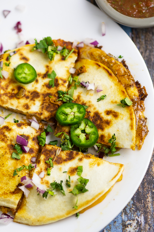 Quesadilla on a white plate topped with fresh jalapeno slices, cilantro, and red onion on a white plate