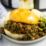 Sloppy joe with a toasted bun sitting on a small plate in front of a Crock Pot