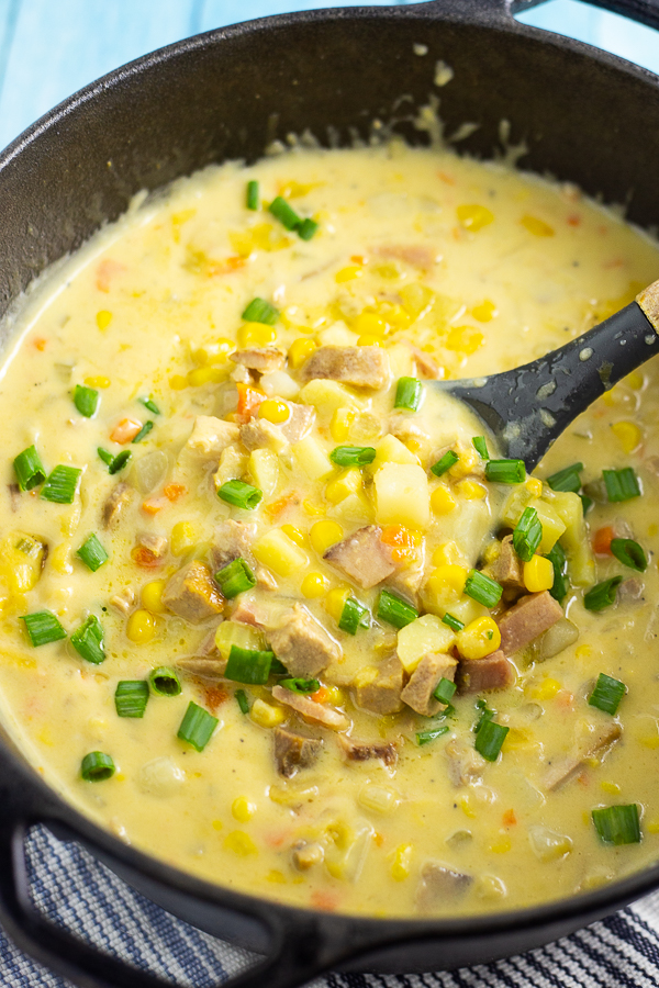 Close up photo of cheesy ham and corn chowder in a cast iron dutch oven with a ladle in the middle.