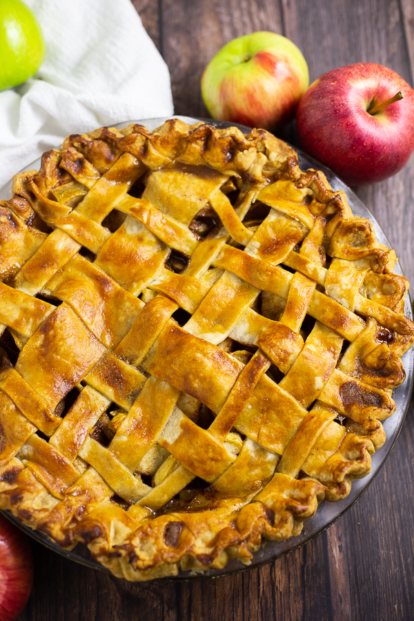Overhead picture of a whole apple pie with a lattice crust surrounded by apples on a rustic wood background
