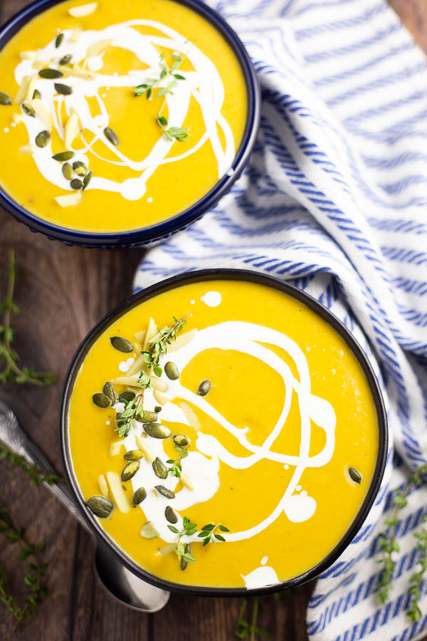 Butternut Squash Bisque in a matte black bowl with a swirl of cream and pepitas and fresh thyme on top sitting on a white and blue linen and a rustic wood background.