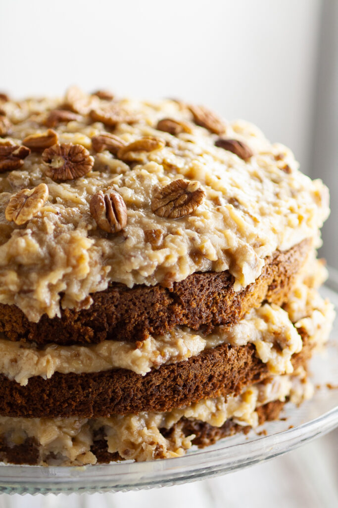 Close up of a German Chocolate Cake topped with coconut pecan frosting and toasted pecans with frosting in between each layer