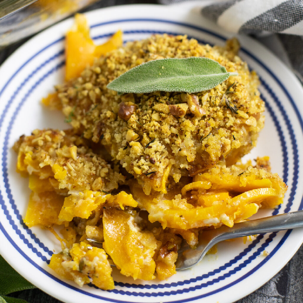 Overhead view of butternut squash gratin on a small glass plate topped with a fresh sage leaf.