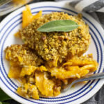 Overhead view of butternut squash gratin on a small glass plate topped with a fresh sage leaf.