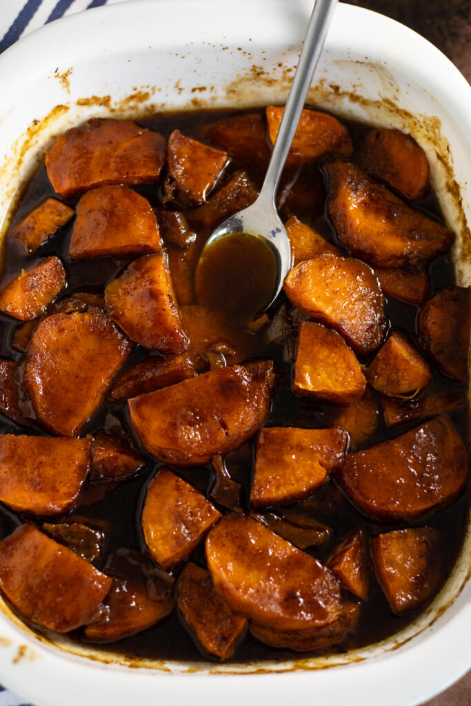 Overhead view of candied sweet potatoes in a white casserole dish with a metal spoon in the middle.