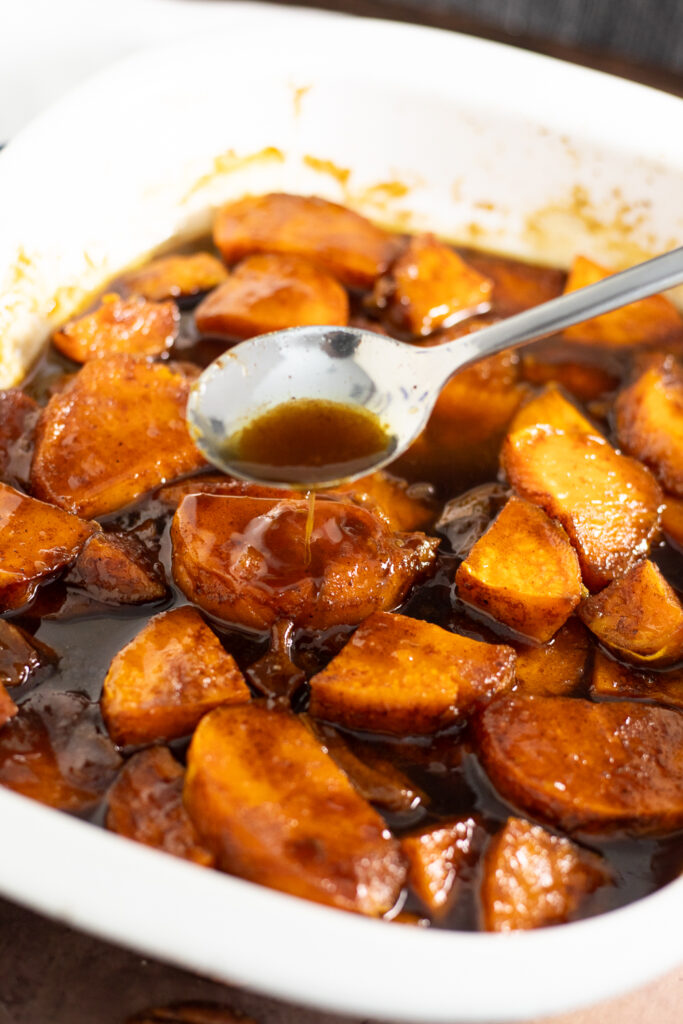 A spoon drizzling buttery brown sugar sauce over candied sweet potatoes.