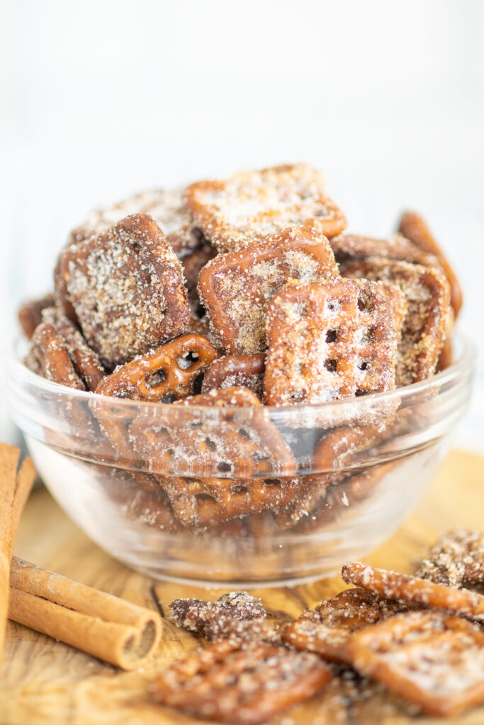A glass bowl full of cinnamon sugar pretzels on a wooden cutting board next to more pretzels and cinnamon sticks.