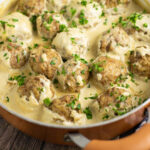 Swedish meatballs in a copper skillet with creamy brown gravy and fresh parsley on top.