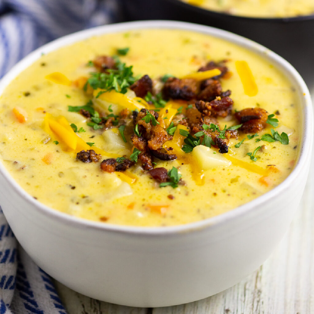 White matte bowl of Cheeseburger Soup topped with shredded cheese, chopped parsley, and crumbled bacon