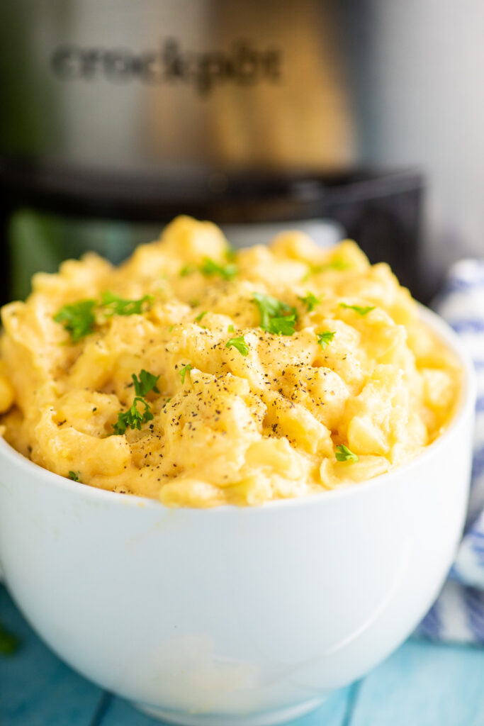 Big bowl full of Crock Pot Mac and Cheese topped with green onions and black pepper in front of a slow cooker