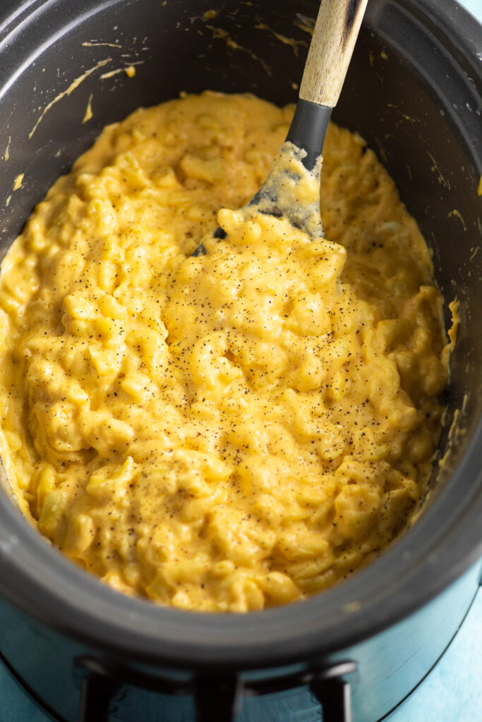 Crock Pot filled with mac and cheese with a wooden spoon stuck in the center