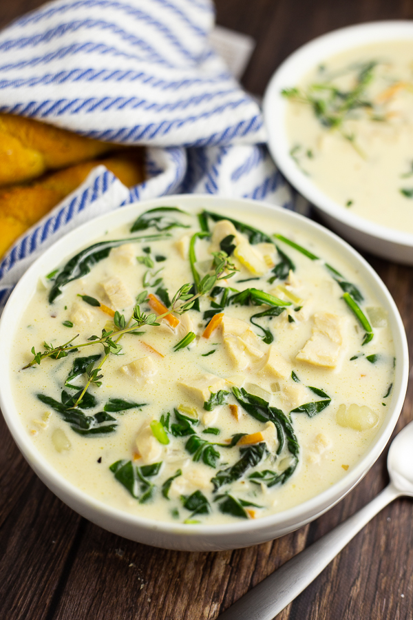 Chicken Gnocchi Soup in a white bowl with a rustic wood background and breadsticks in a white and blue striped linen behind it.