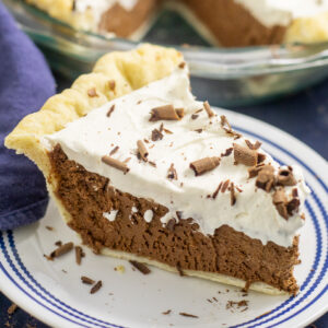A slice of French silk pie on a small plate with a navy blue linen napkin and the remaining pie behind.