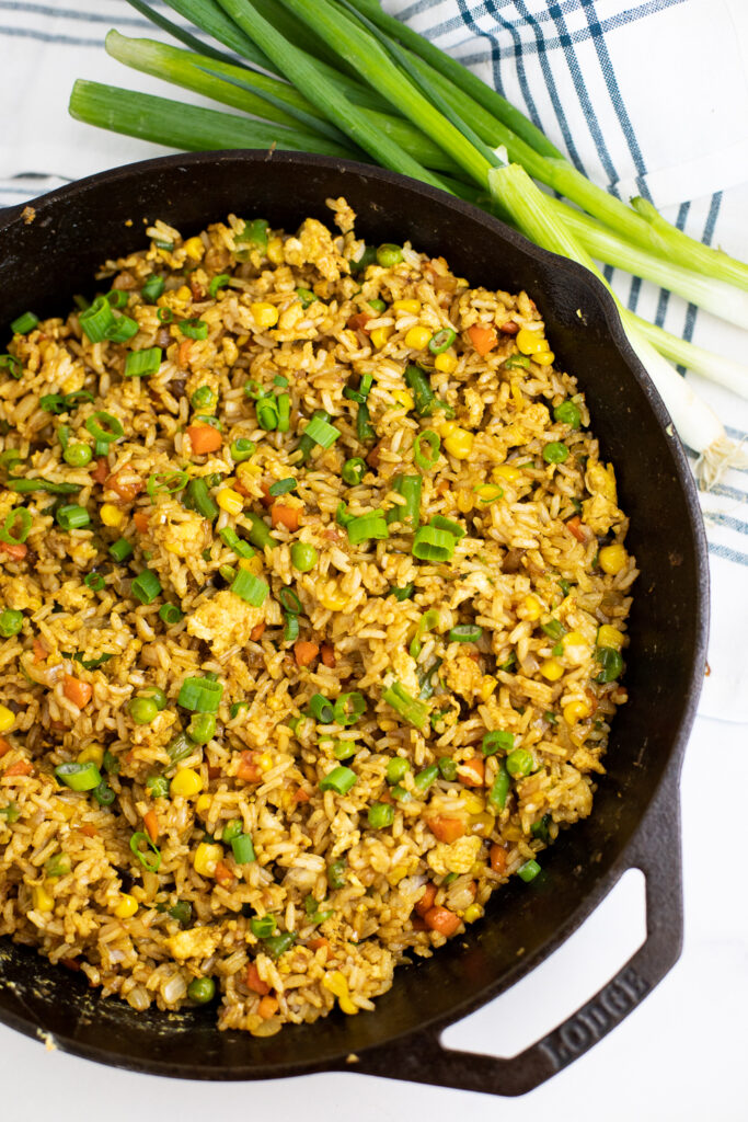 Easy Fried Rice in a cast iron skillet topped with sliced green onions. Skillet is next to a linen napkin and whole green onions