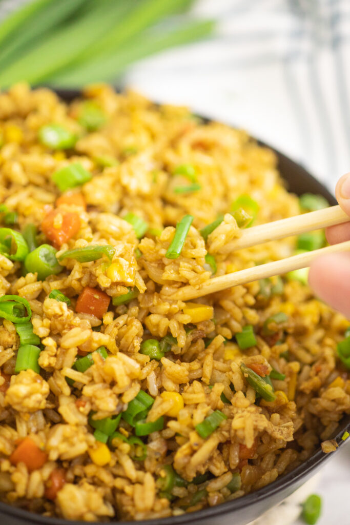 Close up of chopsticks picking up a bite of easy fried rice topped with green onions.