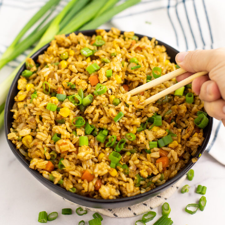 Overhead view of a black bowl full of easy homemade fried rice topped with green onions with chopsticks taking a bite out.