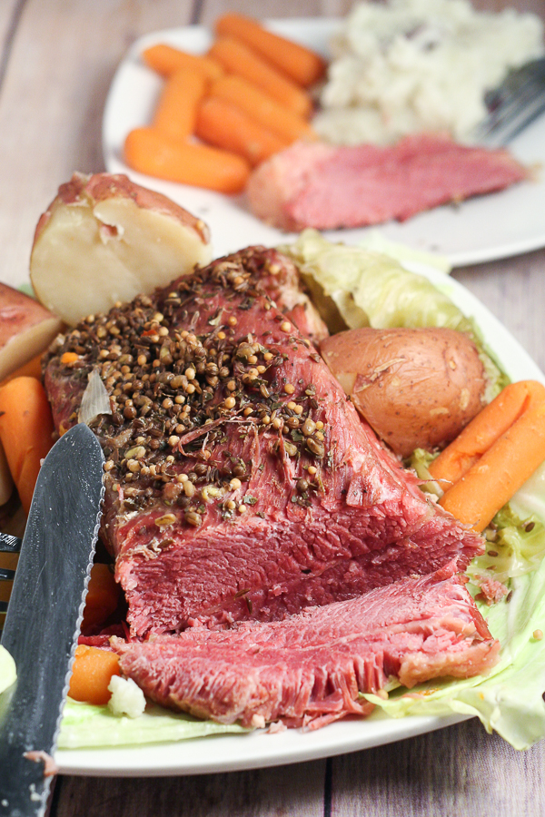 Corned Beef with potatoes and baby carrots on a white plate.