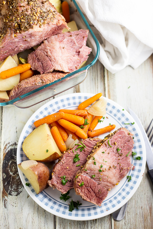 Corned beef, potatoes, and carrots on a white and blue checkered plate on a white wood background