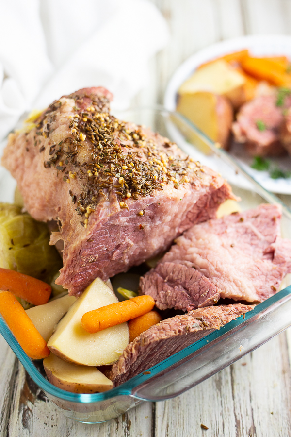 Corned beef with potatoes and baby carrots in a baking dish on a white wood background