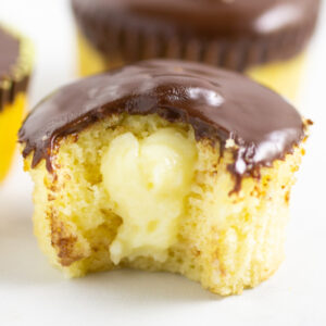 Close up picture of a Boston Cream Pie Cupcakes with a bite taken out on a marble background.