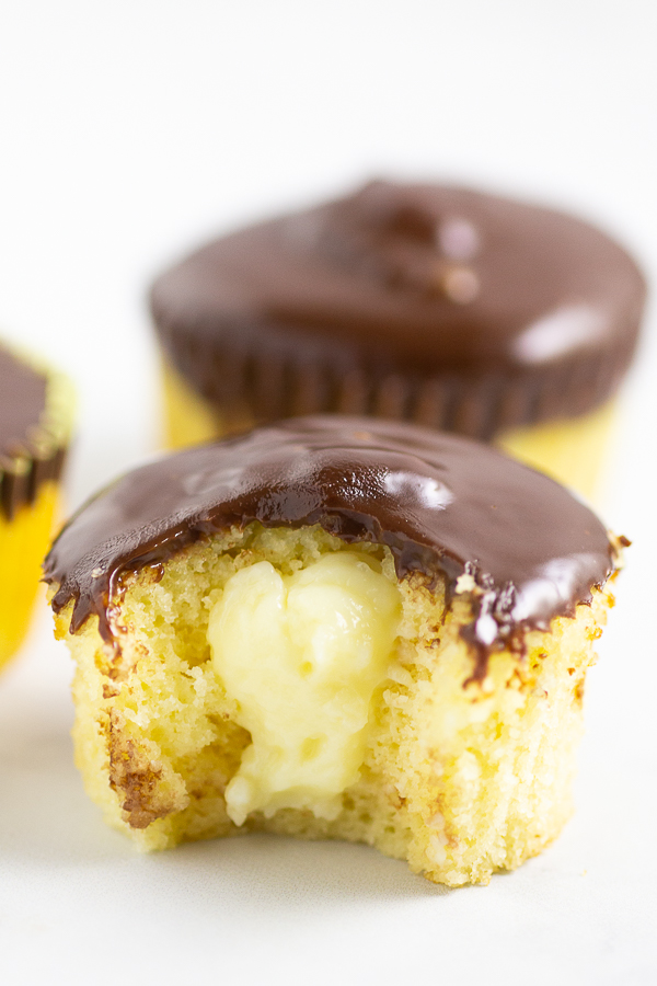 Boston Cream Pie Cupcake with a bite taken out and custard showing sitting on a marble counter.