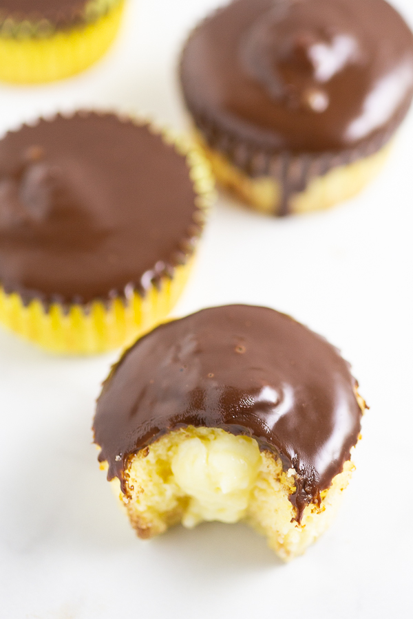 Overhead view of a Boston Cream Pie Cupcake with a bite taken out surrounded by more cupcakes on a marble counter.