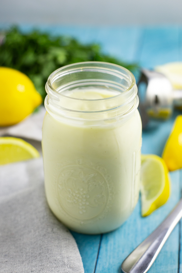 homemade mayo in a mason jar on a bright blue background with lemon wedges