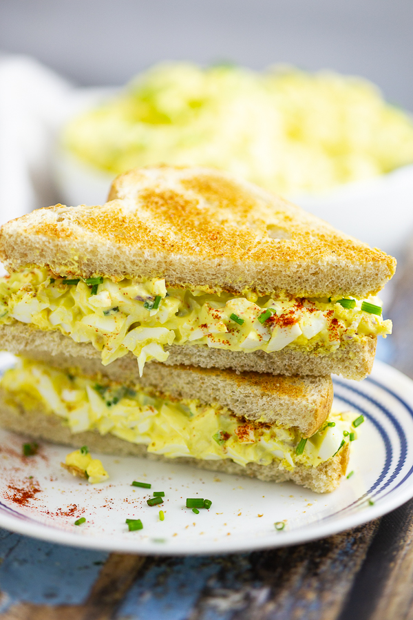 Classic egg salad sandwiches on toasted bread on a plate with a rustic wood background