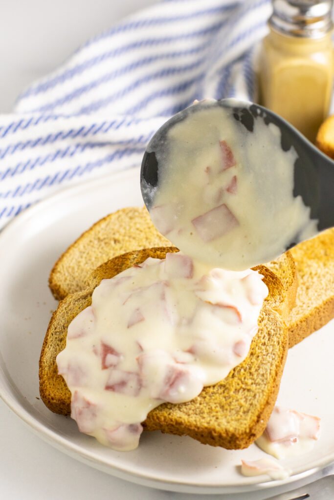 Creamed chipped beef being ladled onto a piece of toast on a small plate