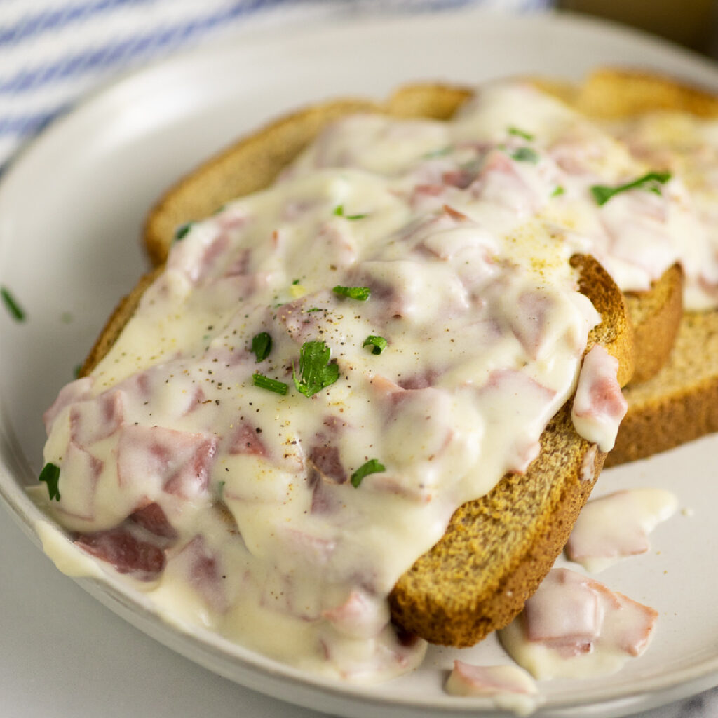 Creamed chipped beef over three pieces of toast topped with black pepper and freshly chopped parsley