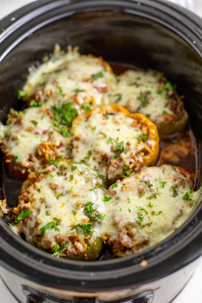 Six crock pot stuffed peppers in a large slow cooker topped with melted cheese and freshly chopped parsley