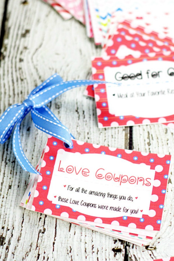 Free Printable Love Coupon book tied together with blue ribbon sitting on a white wood background