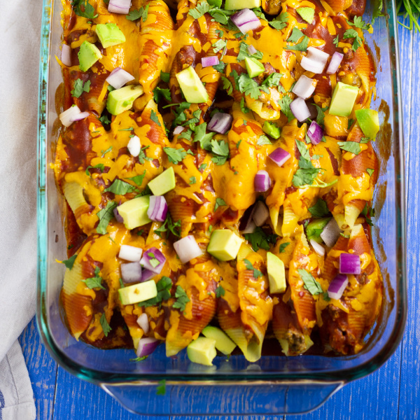 Casserole dish filled with taco stuffed shells topped with fresh avocado, red onion, and cilantro