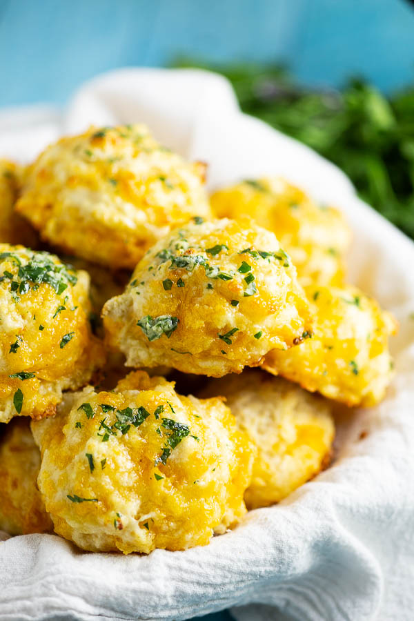 Cheddar Bay Biscuits in a white linen with an aqua background with fresh parsley