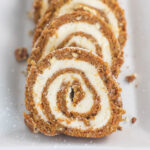 Slices of carrot cake roll lined up and slightly overlapping on a white rectangular plate.