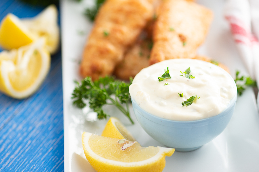 Homemade tartar sauce in a blue bowl with lemon wedges around